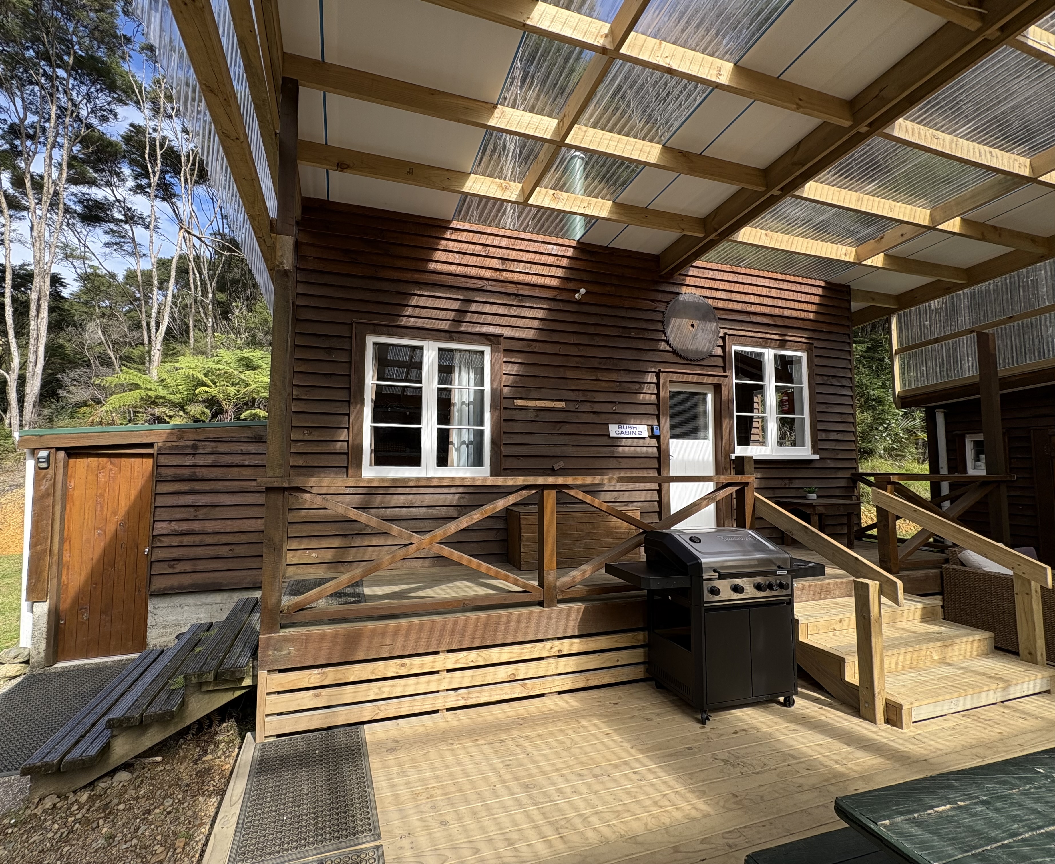 Rustic off-grid timber eco cabin nestled deep within the native forest at Whitestar Station, featuring a large covered veranda and surrounded by lush green bush