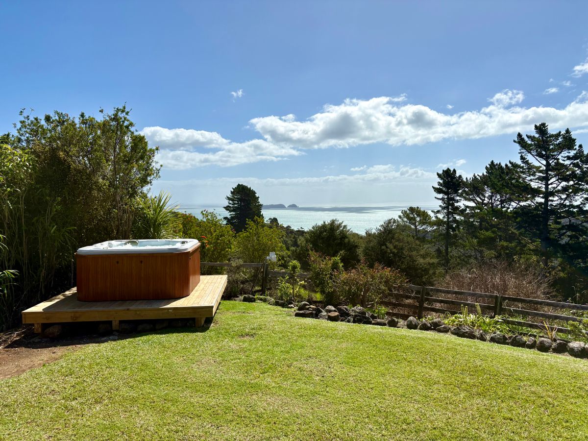Private outdoor spa pool on a raised timber platform at Whitestar Station's Ocean View Retreat, offering panoramic views of the Hauraki Gulf and Coromandel hills.